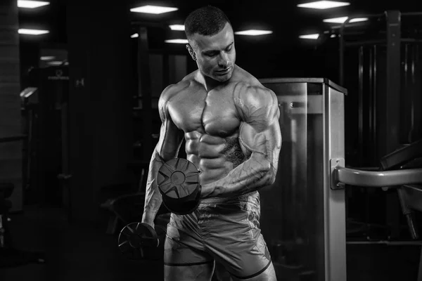 Bel homme avec de gros muscles, posant à la caméra dans la salle de gym — Photo