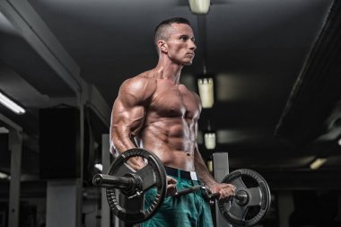 Yakışıklı ve kaslı bir adam, spor salonunda kameraya poz veriyor.