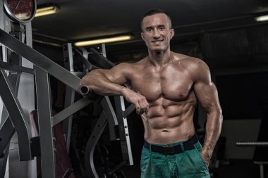 Yakışıklı ve kaslı bir adam, spor salonunda kameraya poz veriyor.