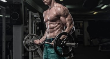 Yakışıklı ve kaslı bir adam, spor salonunda kameraya poz veriyor.