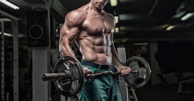 Yakışıklı ve kaslı bir adam, spor salonunda kameraya poz veriyor.