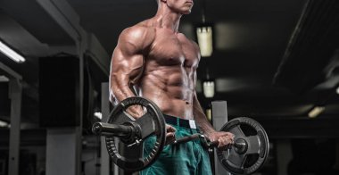 Yakışıklı ve kaslı bir adam, spor salonunda kameraya poz veriyor.