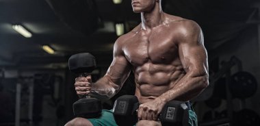 Yakışıklı ve kaslı bir adam, spor salonunda kameraya poz veriyor.