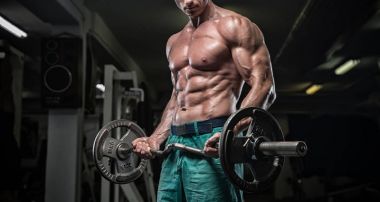Yakışıklı ve kaslı bir adam, spor salonunda kameraya poz veriyor.