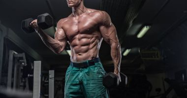 Yakışıklı ve kaslı bir adam, spor salonunda kameraya poz veriyor.