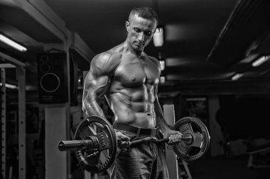 Yakışıklı ve kaslı bir adam, spor salonunda kameraya poz veriyor.