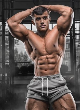 Yakışıklı ve kaslı bir adam, spor salonunda kameraya poz veriyor.