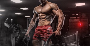 Kaslı vücut geliştirmeci adam spor salonunda dumbbells ile yapıyor