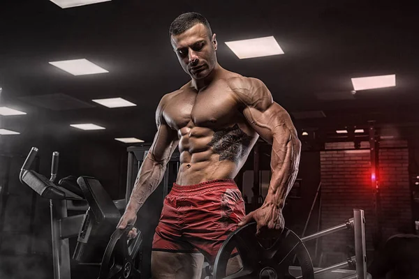 Kaslı vücut geliştirmeci adam spor salonunda dumbbells ile yapıyor — Stok fotoğraf