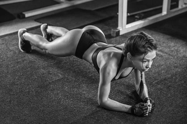 Atractiva joven mujer está haciendo ejercicio de tablón mientras hace ejercicio —  Fotos de Stock