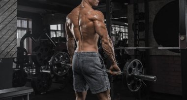 Karanlık bir arka plan üzerinde spor salonunda egzersiz yapan yakışıklı erkek bizi