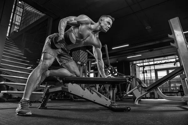Izmos, fiatal férfi súlyemelés edzőteremben sötét háttér. — Stock Fotó