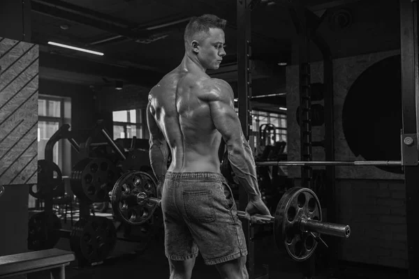 Hombre guapo haciendo ejercicios en el gimnasio sobre un fondo oscuro, nosotros — Foto de Stock