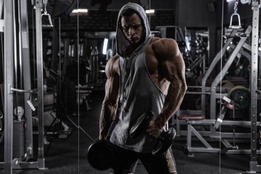 Kas yığını atletik vücut geliştirici adam spor salonunda koyu arka planda, halterli dramatik ışık altında sıkı çalışıyor.