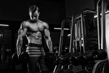 Kas yığını atletik vücut geliştirici adam spor salonunda koyu arka planda, halterli dramatik ışık altında sıkı çalışıyor.