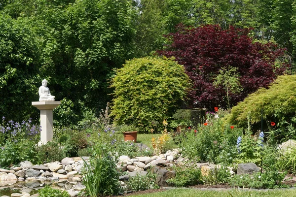 Garden landscape with bushes, garden pond and Buddha statue