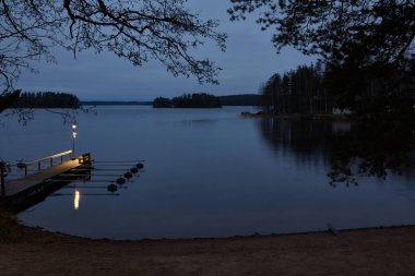 Bulutlu havada gölde şafak söküyor. İskelede fener var..