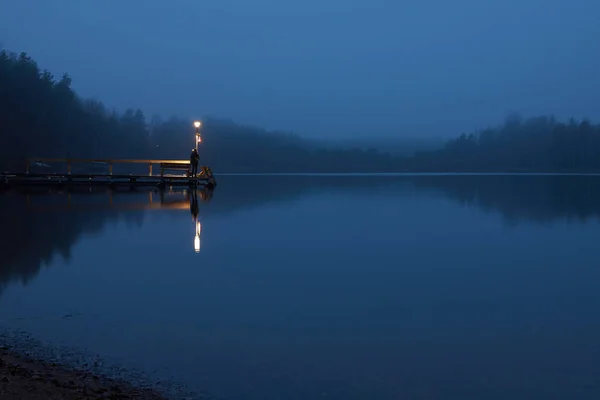 Amanhecer no lago no nevoeiro. Lanterna na doca . — Fotografia de Stock