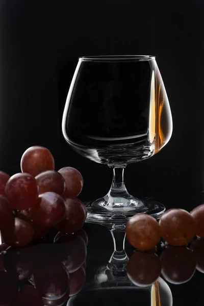 Konjakk på glassveggen på mørk bakgrunn med druer – stockfoto