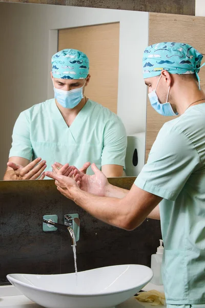 Surgeon looks at the cleanliness of his hands after washing under a stream of water. The right way to wash your hands under running water. Surgeon is cleaning his hand with soap. Hygiene before working with pacietns. A way to not get infected with a