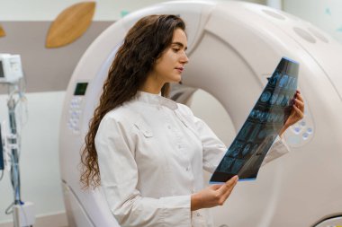 Tıbbi önlüklü genç kadın doktor bilgisayarlı tomografiden sonra hastanın röntgen fotoğrafına bakıyor. Tıp kliniğinde CT taraması