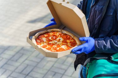 Karton kutuda salamlı ve peynirli pizza. Restorandan mavi tıbbi eldivenlerle güvenlik teslimatı. Coronavirus covid 19 'u durdurmak için karantina. Terfi metni için sol taraf boş