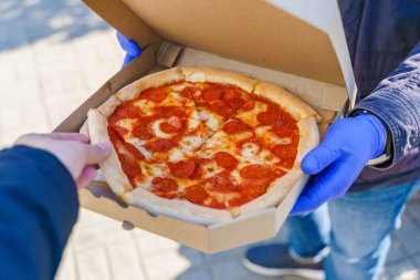 Müşteri karton kutudan bir dilim pizza alır. Coronavirus covid 19 'u durdurmak için tıbbi eldiven içinde yiyecek teslimatı..