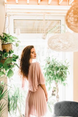 Profesyonel model pencerenin karşısında duruyor ve sağ tarafa bakıyor. Uzun dalgalı saçlı doğal güzel kadınlar..