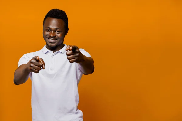 Happy african man points to camera. Motivation from black sportsman. Bearded motivated man on orange isolated background with empty space in right side
