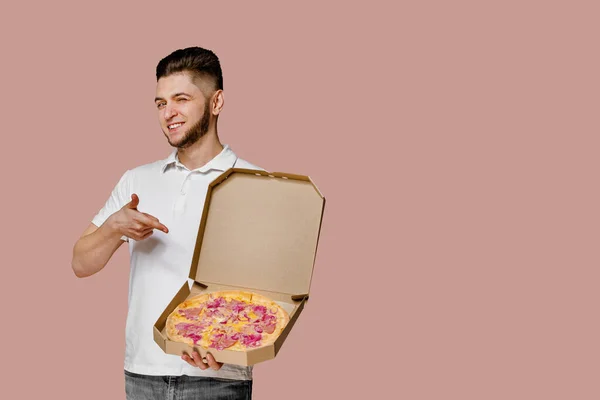 Handsome yound courier with points to pizza. Empty space for text advertise. Safery delivery from restaurant. Confident student works courier at quarantine period. Save your life and stay at home.