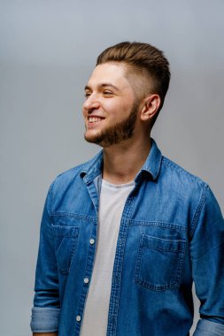 Genç yakışıklı adam beyaz arka planda duruyor ve berber dükkanını ziyaret ettikten sonra gülümsüyor. Kendine güveni tam bir adam sıradan bir kot gömlek giyer ve kameraya bakar. Sakallı beyaz iş adamı..