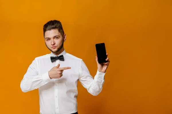 Call to safety delivery. Smartphone advertise. Professional model points to phone for advertise of on-line business at quarantine period. Show man. Handsome man wears white shirt with butterfly.