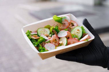 Dana etli yeşil salata ve berduşlar. Karantinada maskeli ve siyah eldivenli güvenlik teslimatı. Eko termik kutuda salata. Restorandan gelen sipariş, evde kalan insanlara iletiliyor..