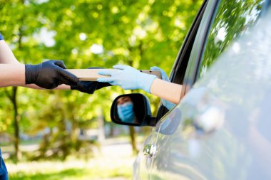 Karantina Coronavirus sırasında pizzacının vitrininden güvenli pizza teslimatı. Mavi tıbbi eldivenlere sarılı eller karton kutuya yemek koyar. Sosyal mesafelere göre otomobille teslimat
