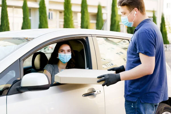 This is so big pizza. Big size pizza in carton eco box. Courier gives large pizza to young business woman. Girl in medical mask and gloves gets huge pizza in car. Delivery by car. Stay at home
