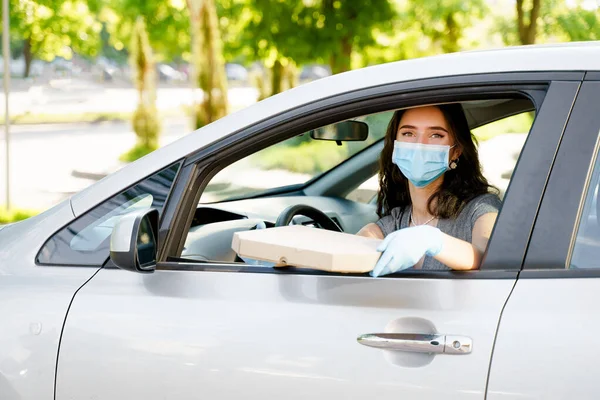 Pretty young girl seats in car and gets georgian cheese pastry from courier. Woman in medical mask and gloves. Georgian hot food delivery. Stay at home at quarantine covid 19. Delivering by car