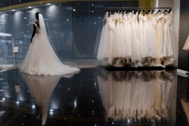 İpek şifon, tül ve dantelden yapılmış gelinlik giymiş aptal. Düğün dükkanının içinde. Düğün salonundaki askılarda beyaz krem gelinlik. Kollarında inciler ve kristaller var..