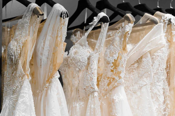 Wedding dresses made of silk chiffon, tulle and lace. Beautiful White cream bridal dress on hangers in wedding salon. Pearls and crystals pendants on the sleeves of a delicate color of a wedding dress