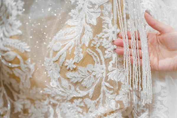 花嫁はハンガーの豪華な白いクリームの結婚式の服に触れる シルクシフォン チュールとレースで作られたドレス ウェディングドレスの繊細な色の袖に豪華な真珠とクリスタルペンダント — ストック写真