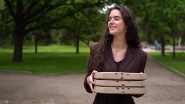 Pizzacıdan yemek servisi. Yeşil parkta üç pizza kutusu ve gülümsemeyle yürüyen bir kız. 2 + 1 pizza teslimatı reklamı. Güvenli fast food teslimatı. Bir pizza bedava.. 