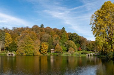 Wiltshire 'daki Stourhead bahçesindeki gölün etrafındaki sonbahar renklerinin görüntüsü.