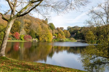 Wiltshire 'daki Stourhead bahçesindeki gölün etrafındaki sonbahar renklerinin görüntüsü.