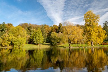 Wiltshire 'daki Stourhead bahçesindeki gölün etrafındaki sonbahar renklerinin görüntüsü.