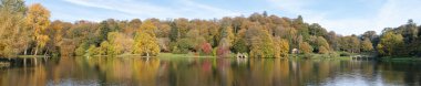 Wiltshire 'daki Stourhead bahçesindeki gölün etrafındaki sonbahar renklerinin panoramik fotoğrafı..