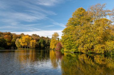 Wiltshire 'daki Stourhead bahçesindeki gölün etrafındaki sonbahar renklerinin görüntüsü.