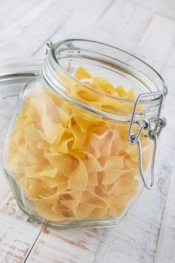 Bardaktaki çiğ makarna ahşap bir zemine karşı.