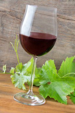 Ahşap arka planda kırmızı şarap ve asma yaprakları