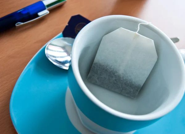 Break tea bag in cup with wooden background