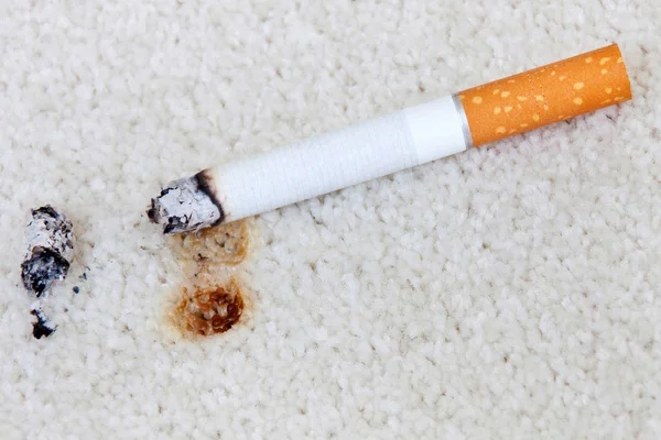 Brennende Zigarette auf Teppich mit Loch — Stockfoto