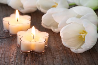 Ahşap zemin üzerinde beyaz laleler olan Paskalya dekorasyon mumları.